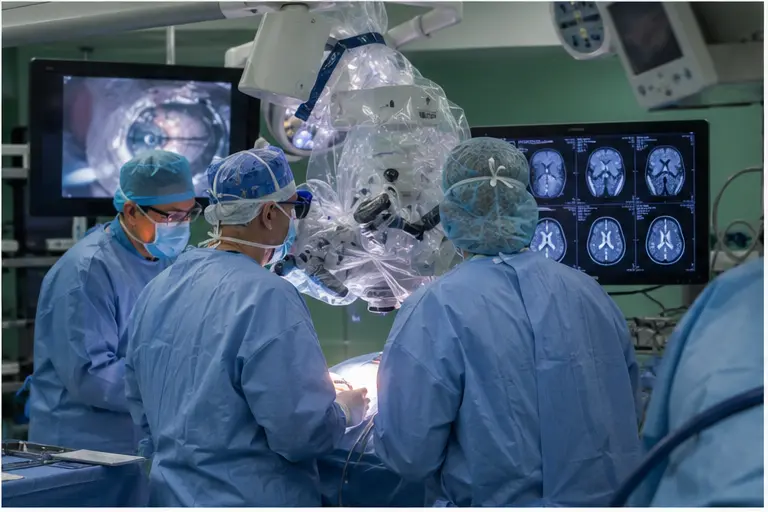 Equipe di neurochirurgia utilizza microscopio e monitor in sala operatoria